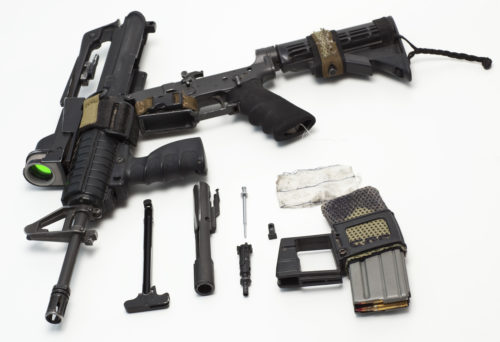 Disassembled M16 short rifle on white table.